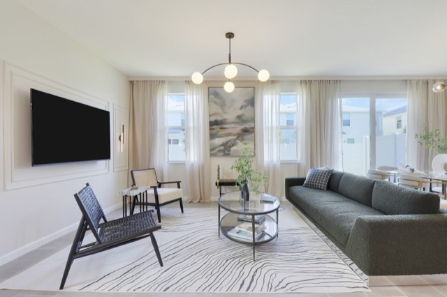 Living room with a green sofa, two rear windows with sheer curtains and the sliding door at the right