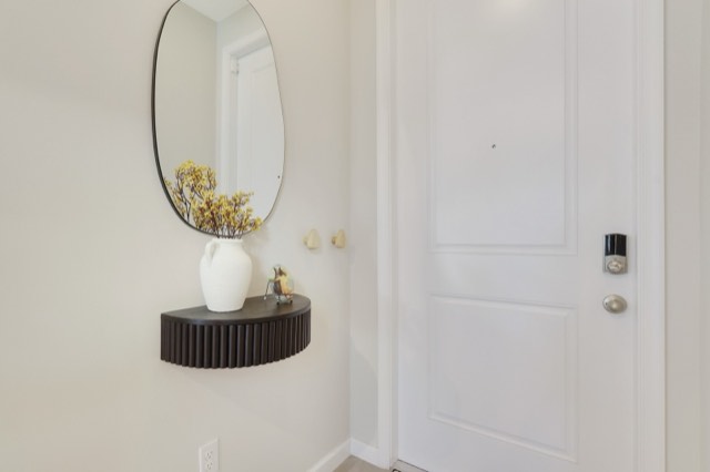 Foyer with the front door and its keypad lock, a fluted wall shelf and an organic-shaped mirror