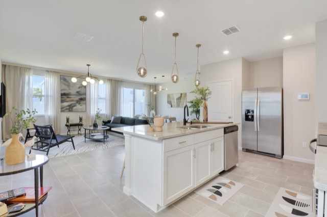 Open kitchen with a white island and stainless refrigerator, the living room and its windows beyond