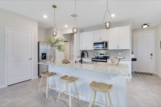 Kitchen island with three wood stools and the sink, the range wall behind it and the front door at the far right