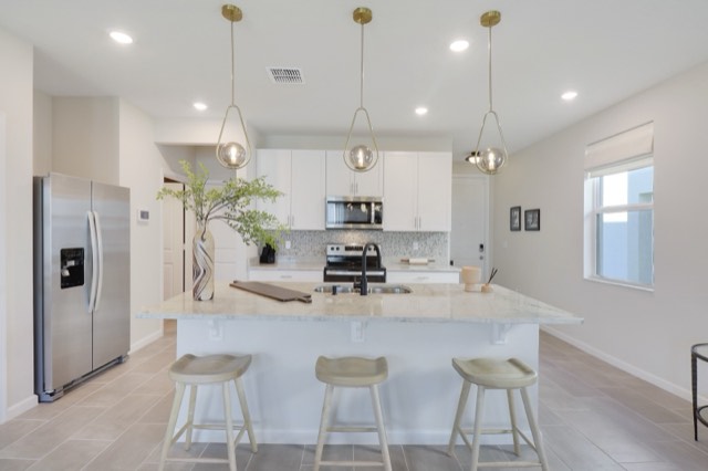 Kitchen from the side: the stainless refrigerator at the left, the island with three stools in front