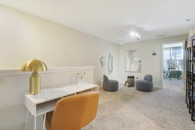 Loft desk nook with a white terrazzo-look desk, a brass lamp and a tan chair, the loft seating behind