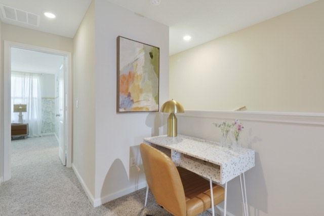 White desk and tan chair against the stair half wall, beside the doorway to a bedroom