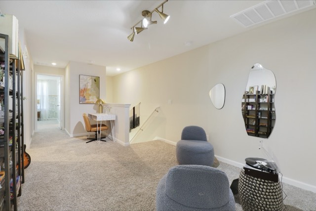 Upstairs loft with brass track lighting, a desk nook against the stair half wall and the hall to the primary bedroom