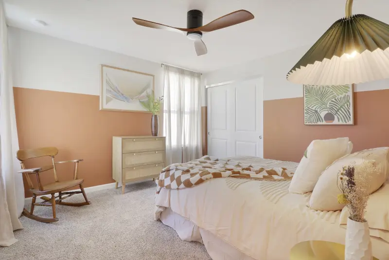 Coral and cream bedroom at 261 Osprey Preserve with a rocking chair, a light wood dresser and a pleated pendant lamp