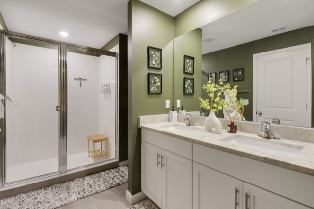 Primary bath with olive walls, a white two-sink vanity and a framed glass shower
