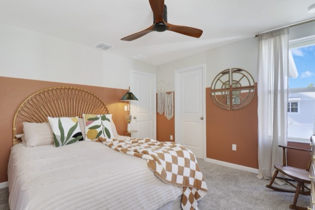Coral and cream bedroom with a rattan headboard, seen from the window side, a round wall mirror above the chair