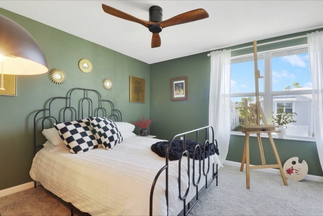 Sage-green bedroom with a black metal bed, a wide window and an easel