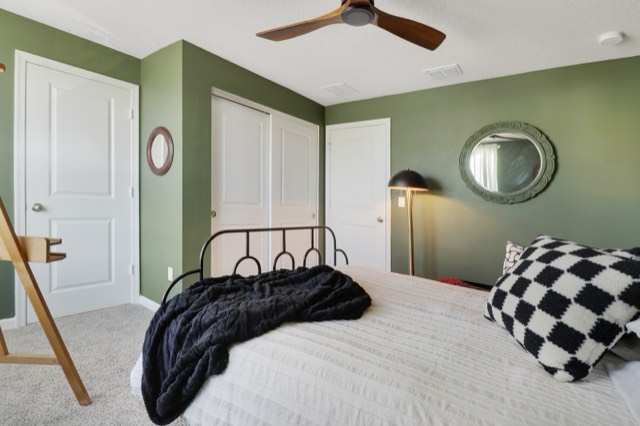Sage-green bedroom from the foot of the bed, a round mirror and the closet doors behind