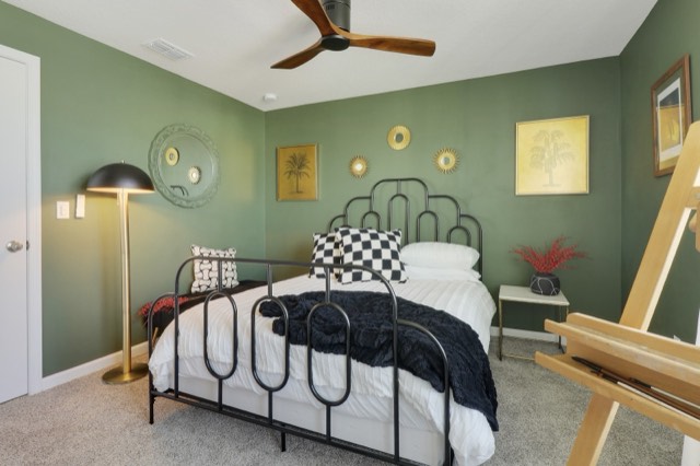 Sage-green bedroom with a brass floor lamp beside the black metal bed and an easel at the right