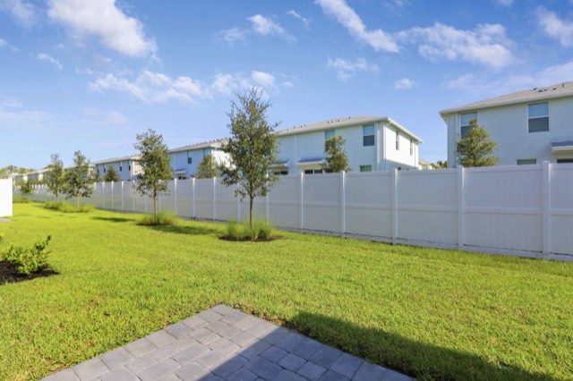 Backyard lawn enclosed by a white vinyl fence, neighboring two-story townhomes beyond