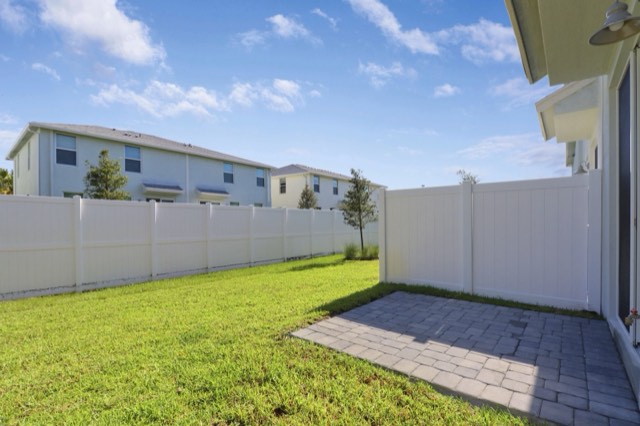 Small paver patio against the back of the house, with lawn and a white vinyl privacy fence