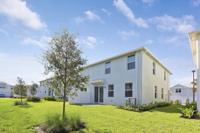 Rear of a two-story light-colored townhome building with a young tree on the lawn