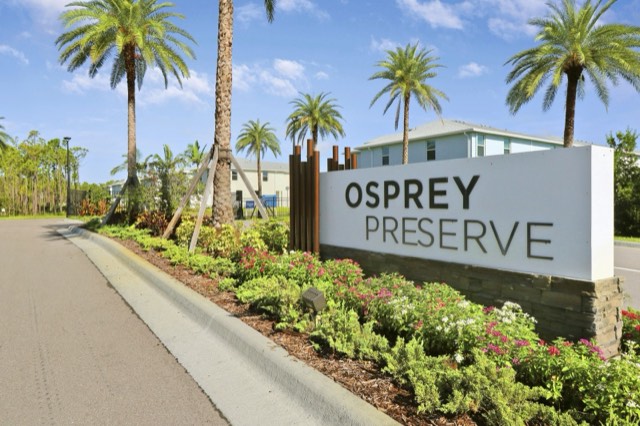 Osprey Preserve entrance sign among palms and flowering plantings, the entry road at the left
