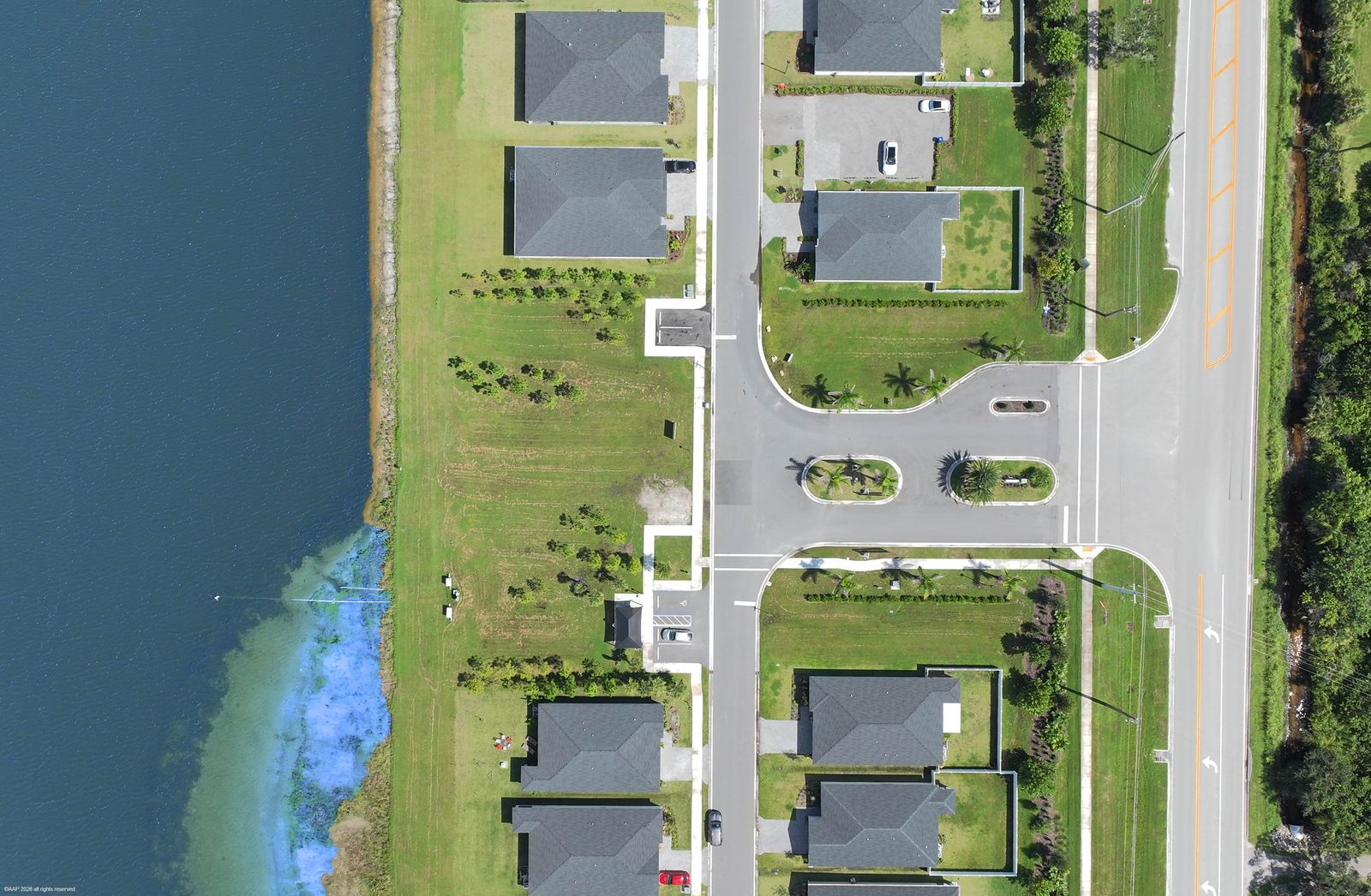 Straight-down aerial of the Hampton Park entrance road with landscaped medians, homes on either side and the lake along the left edge